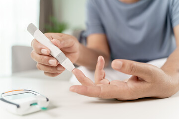 Mature Asian woman using lancet on finger for checking blood sugar level by Glucose meter, Healthcare and Medical, diabetes, glycemia concept