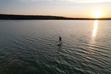Silhouette of people on SUP board and paddling at sunset, light waves on water. Pan shot doing sports in beautiful landscape. Healthy lifestyle. Concept of fitness