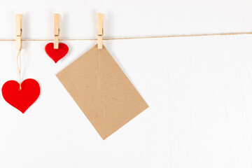 three wooden clothespins hang on a rope on a white background and hold a heart and an envelope. flat lay