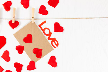 wooden clothespins hang on a rope on a white background and hold a heart and an envelope. many scattered hearts and the word love. selective focus