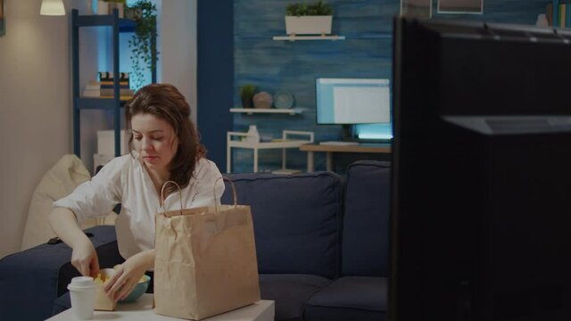 Person Putting Takeout Fast Food Boxes On Table Sitting On Sofa At Home. Caucasian Woman Unpacking Delivery Meal From Bag, Eating Takeaway Snacks While Watching Television In Living Room.