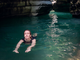 Smiling girl swims in turquoise water in a shady gorge of canyons under the sun's rays