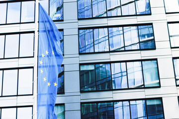 European Union flag waving in front of modern corporate office building, symbol of EU Parliament,...