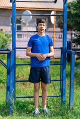 teenage boy exercising outdoors, sports ground in the yard, he posing at the horizontal bar, healthy lifestyle