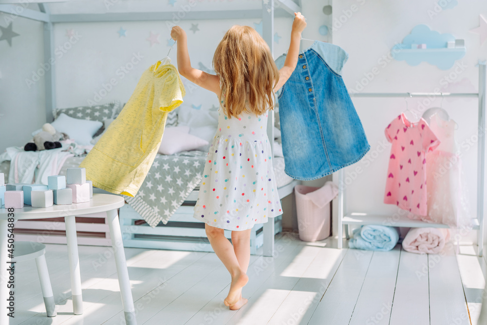 Wall mural beautiful little girl choosing a dress in the kids room