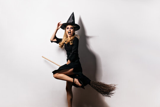 Emotional girl in carnival costume expressing happiness in halloween. Studio portrait of enchanting blonde lady wears magic hat.