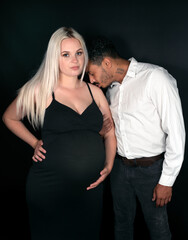 Stylish and happy multi-ethnic couple expecting a baby and kissing lovingly