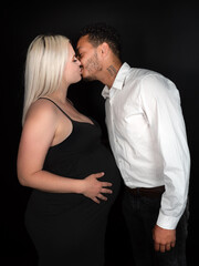 Stylish and happy multi-ethnic couple expecting a baby and kissing lovingly