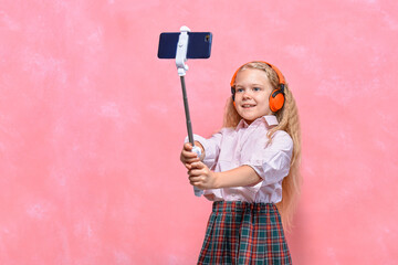 online training. little schoolgirl in headphones learns by smartphone. pink background