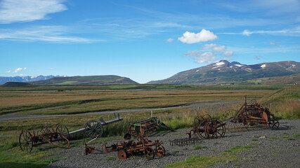 Fototapeta premium old traditional rusty carriage and various other agricultural items in the field, under the cloudy sky, Laufas old farmhouse, Akureyri, Iceland