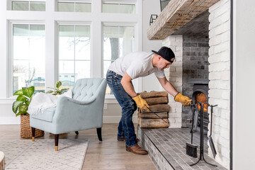 Fototapeta premium An adult male in his 40s loading firewood into a wood burning stove in a modern farmhouse family room.