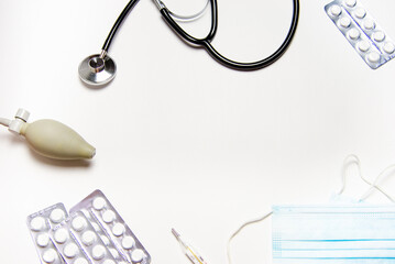 Medical devices are laid out on a white background: stethoscope, tonometer, pills, face mask, thermometer, Copy Space concept