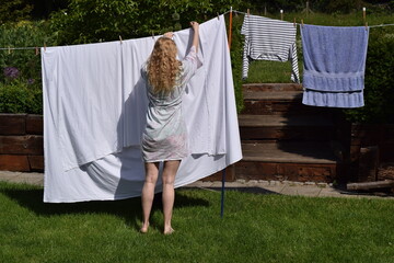 Young woman is hanging linen outside.
