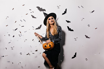 Pleasant young witch posing with bats on background. Pretty blonde vampire girl holding halloween...