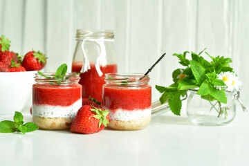 Homemade multi-layer dessert with strawberry and cream cheese in a glass jar. Ripe fresh green lime and mint on white background.
