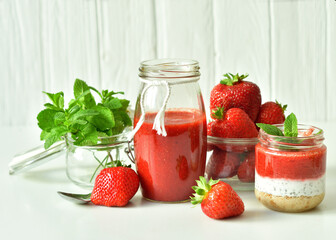 Homemade multi-layer dessert with strawberry and cream cheese in a glass jar. Ripe fresh green lime and mint on white background.
