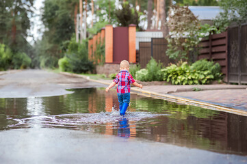 Fototapeta na wymiar Happy toddler walks through the puddles in blue rubber boots with splashes close-up and copy space...