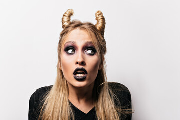 Close-up shot of shocked pretty witch. Interested blonde woman posing at halloween carnival.