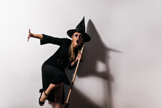Shocked blonde witch posing on white background. Studio portrait of worried woman in halloween wizard costume.