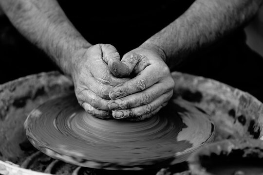 Black and white photo of potter molding clay with his hands on a spinning pottery wheel. Original public domain image from Wikimedia Commons