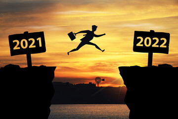 Businessman jumping between 2021 and 2022 years with sunset background	