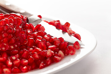 Close-up of organic red pomegranate seed (Punica granatum) in white ceramic plate over white background.