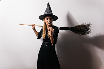 Angry witch thinking about something evil. Studio shot of female wizard in long black dress expressing rage in halloween.