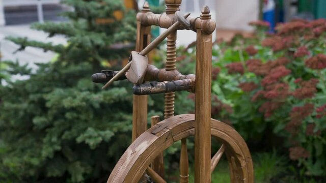 A wooden spinning wheel is on the grass in the yard. A tool on which threads were spun. Vertical placement of the wheel on top of which there is a kuzhivka. The subject of folk life for spinning