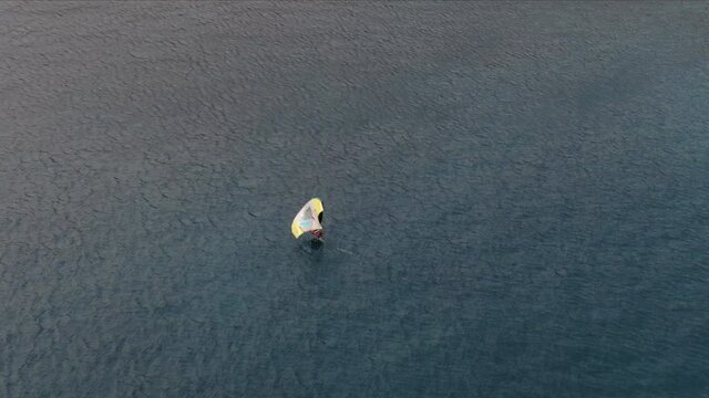 drone shot from behind on man doing windsurfing in the sea.