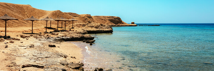 Sandy and rocky coast with palm beach umbrellas. Desolate resort beach on the coast shore of Red...