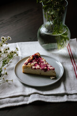 A slice of pie with farmer cheese and raspberries with some field flowers on a small plate on a piece of table cloth and wooden table