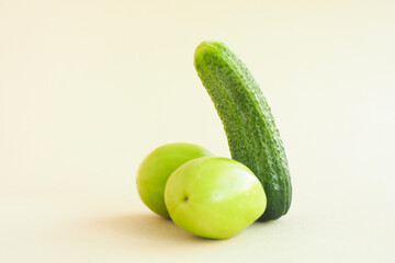 green cucumber and two green tomatoes on a beige background. male penis concept..