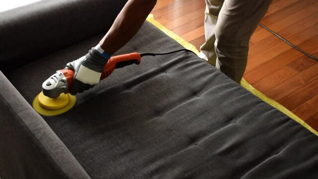 Professional cleaning the sofa with an electric polisher brush.