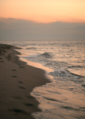Sunset on the coastline. Ocean and sand beach with footprints on it