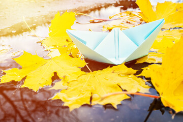 blue origami paper boat over fall leaf background. autumn concept