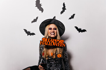 Adorable long-haired woman posing in halloween with bats on background. Wonderful witch girl having...