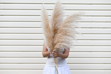 Woman holding a beautiful bouquet with pampas grass on beige background. Front view. Faceless...
