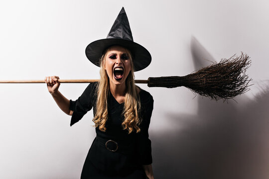 Angry witch with long hair holding broom. Blonde female wizard screaming in halloween.