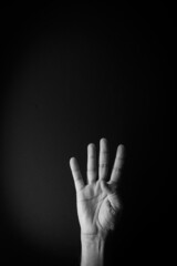 Black and white image of hand demonstrating sign language number four against black background with empty copy space