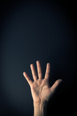 Colour image of hand demonstrating sign language number five against dark background with empty copy space