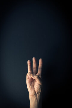 Colour image of hand demonstrating sign language number three against dark background with empty copy space