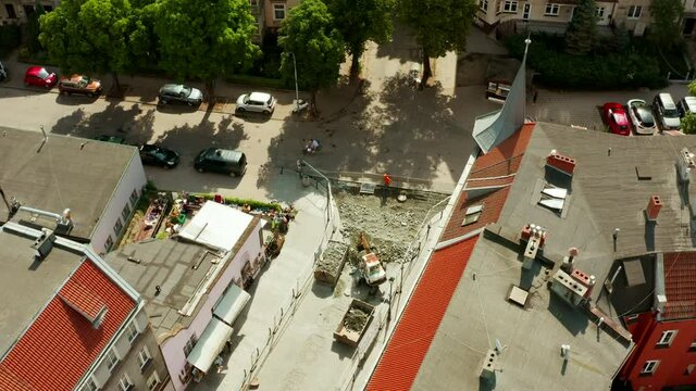 Aerial view of the street of the old city and a small excavator digging paving stones and loading it into a dump truck. Repair of the road and laying of new paving stones and a curb in the old city.