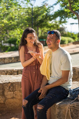 Couple of friends smiling with mobile phone in hand. They are happy in a park. They are Caucasian. They are laughing together. Javea, Alicante.