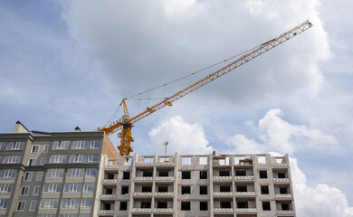 Naklejka premium Construction crane on an unfinished residential building against the sun and blue sky. Housing construction, apartment building in the city. Construction site of residential buildings.