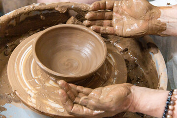 The hands of the master potter form an earthen vessel on the potter's wheel. A potter works in a pottery workshop with clay. Close-up.