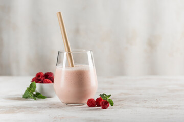 A glass with a Lassi drink with raspberries, mint and a bamboo tube on a light background.