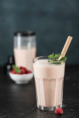 Lassi drink with raspberries in a glass with mint and a bamboo tube, with a cocktail shaker on a dark background.