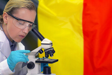 Female biochemist mixing substances to study under the microscope against Belgium flag background. Medical technology and pharmaceutical research and development of science concept in Belgium
