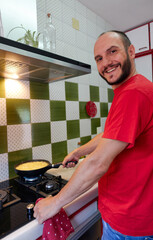 man frying potatoes in frying pan and looking at camera smiling