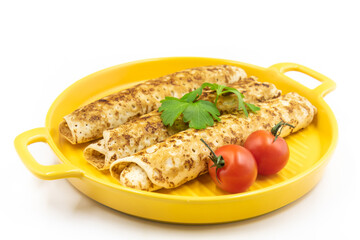 Pancakes rolls on a yellow plate with parsley and tomatoes.